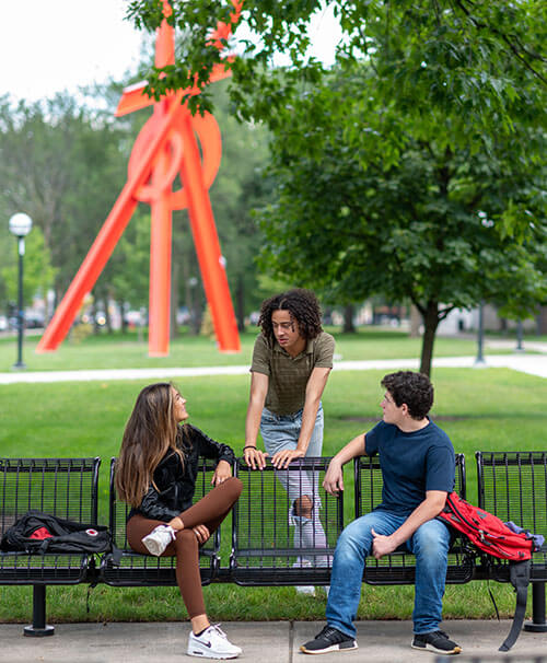 Students talking on a bench in front of the Orion sculpture