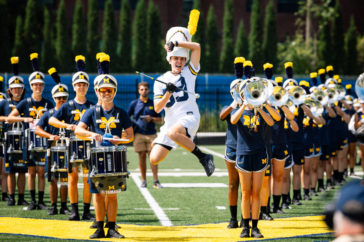 The Michigan Marching Band on the field with the drum major jumping